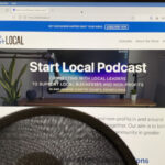 A recording mic in front of a computer monitor showing the Start Local podcast website