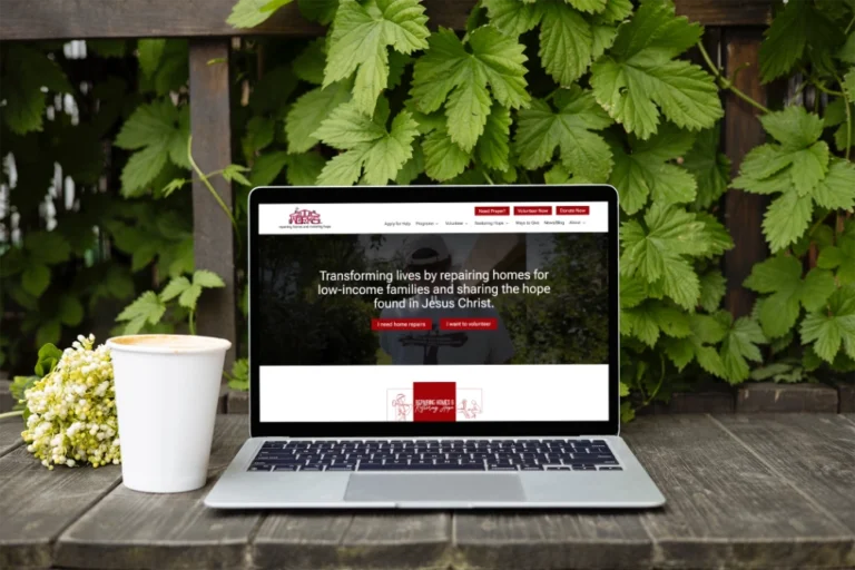 The Good Works website loading on a laptop, resting on a deck and next to a cup of coffee.