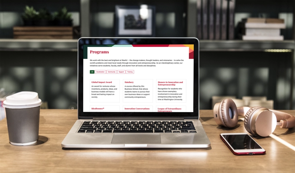 The Program page on the Skandalaris Center website as shown on a MacBook. which is resting on a wooden desk.